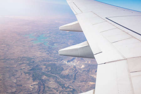 Wing of an airplane flying above perfect lake landscape