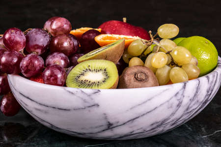 Basket of fresh tropical fruitson in bowl on black marble background. Pineapple, papaya, mango, kiwi, grape, garnet, tangerines, bananas, apples, watermelon slices, pitaya or dragon fruitの写真素材