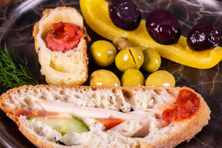 Close-up photo of a sandwich. Sandwich with meet, prosciutto, salami, salad, vegetables, lettuce, tomato, onion and mustard on a fresh sliced rye bread on wooden background. Olives background.の写真素材