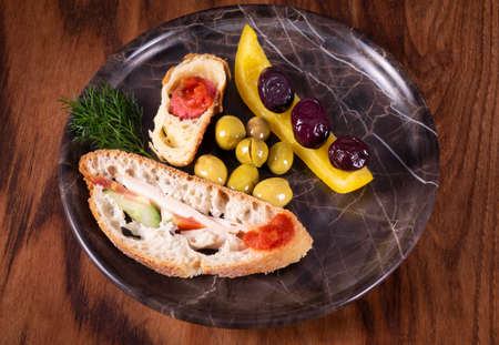 Close-up photo of a sandwich. Sandwich with meet, prosciutto, salami, salad, vegetables, lettuce, tomato, onion and mustard on a fresh sliced rye bread on wooden background. Olives background.の写真素材