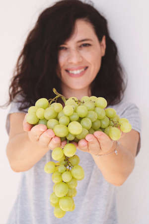 Beautiful woman, holding fresh green grape in handful, isolated on white background. Vertical image
