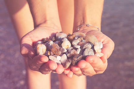 Young woman holding on her hand the beautiful colorful pebbles of Greek beaches.