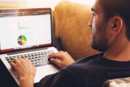 Young man sitting on sofa, working on laptop.の写真素材