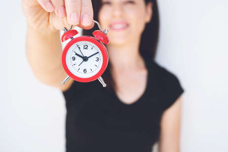 Happy young woman in black t-shirt a holding red alarm clock and waving hand isolated on white