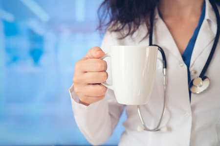Doctor holding coffee cup with stethoscope and looking up in the morning.Young female confident...