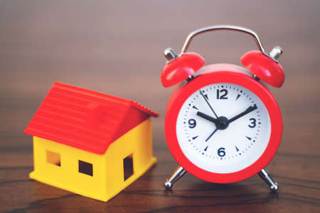 Miniature home and red alarm clock with wooden background