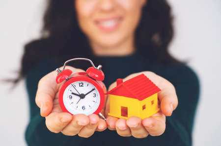Woman hand holding house and alarm clock. house model for finance and banking concept.の写真素材