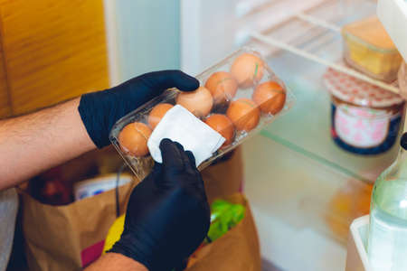 COVID-19: Is it necessary to clean your groceries delivered at home? Man in quarantine wiping plastic package with sanitizing wipes after shopping or receiving online delivery bags and to place in the refrigeratorの写真素材