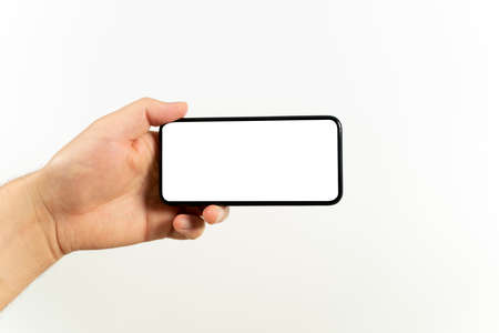 Man hand holding the black smartphone with blank screen and modern frameless design positions horizontal - isolated on white backgroundの写真素材