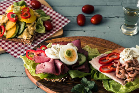 Variety of danish open sandwiches with eggs, seafood and roast beef, lying on wooden boards on a light gray wooden table.の写真素材
