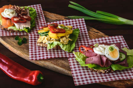 Variety of danish open sandwiches with eggs, seafood and roast beef, lying on checked napkins on a wooden board.の写真素材