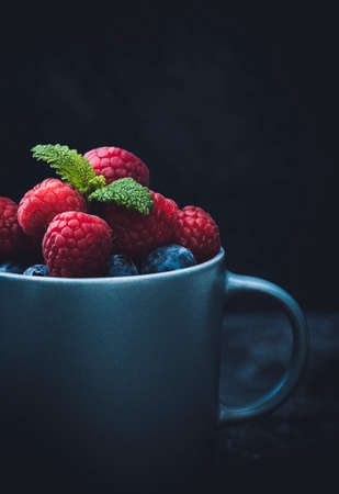 Gray cup filled with raspberries and blueberries, decorated with mint leaves. Closeup.の写真素材