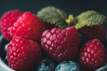 Closeup of raspberries with a few blueberries and mint leaves in the background.の写真素材