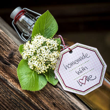 Glass bottle with homemade elderflower syrup lying on an old wood truss.の写真素材