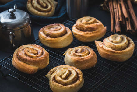 Homemade cinnamon rolls on a colling rack with cinnamon sticks and old vintage silver sugar bowl.の写真素材