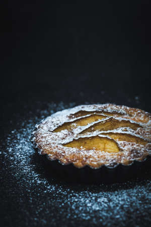 Apple tartlet on a black table, sprinkled with powdered sugar. Vertical closeup with copy space.