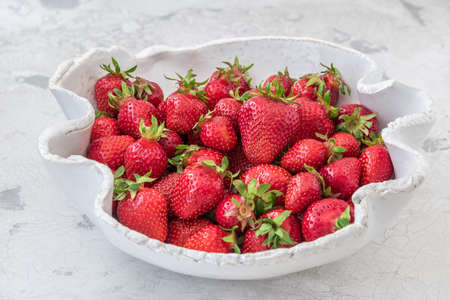 Handmade white pottery bowl with fresh strawberries on white backgroundの写真素材