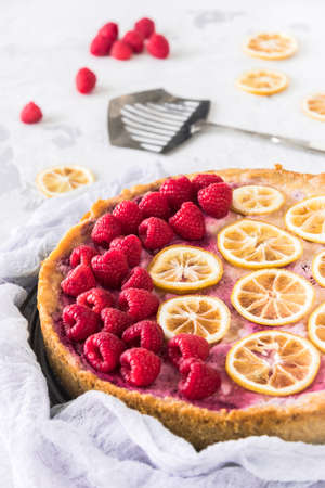 Cheese cake with raspberries and dried lemon slices on white background, some raspberries, lemon...