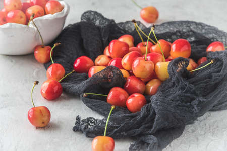 Ripe orange sweet cherries of sort 'royal anne' on a black cloth, white bowl with cherries in the backgroundの写真素材