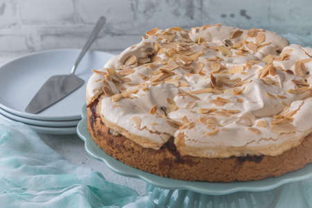 Delicious homemade rhubarb cake on a mint green cake plate, topped with sweet meringue and roasted almonds and decorated with summer flower. Mint green cloth and white background.の写真素材