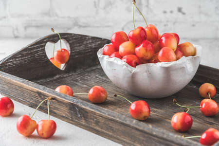 White bowl with ripe orange sweet cherries of sort 'royal anne' on a wooden tray, white backgroundの写真素材