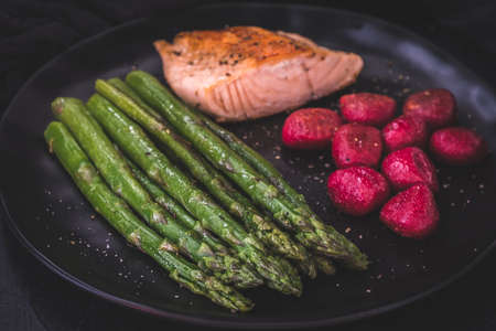 Roasted green asparagus and salmon with beetroot gnocchi on black backgroundの写真素材