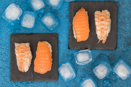 Top view of two slate plates with nigiri sushi and ice cubes on blue backgroundの写真素材