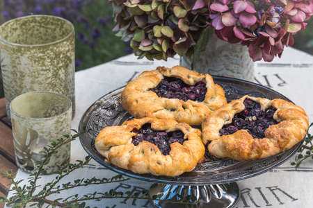 Homemade blueberry galettes on a table with hydrangea flowers and light green glasses for candles. Closeup.の写真素材