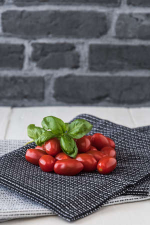 Ripe cherry tomatoes with basil branch on black and white tea towels against a gray stone background. Vertical stock photo.の写真素材