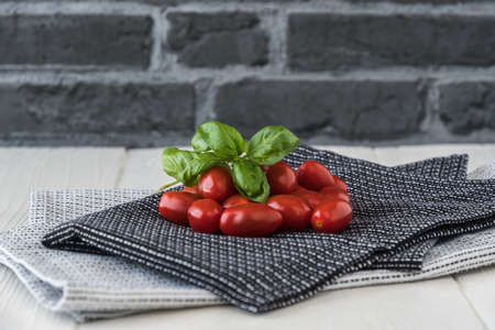 Ripe cherry tomatoes with basil branch on black and white tea towels against a gray stone backgroundの写真素材