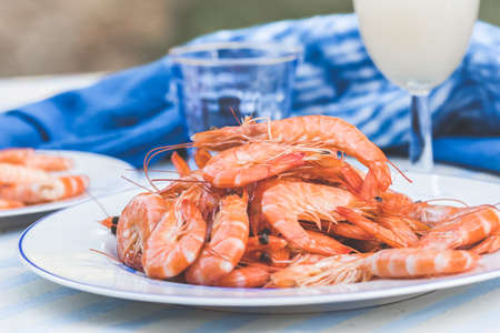 Plate with prawns and a glass with aperitif on a blue and white tableの写真素材
