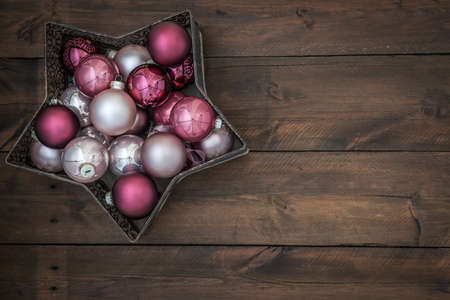 Star-shaped bowl filled with pink and silver christmas baubles. On wooden background with copy space.の写真素材
