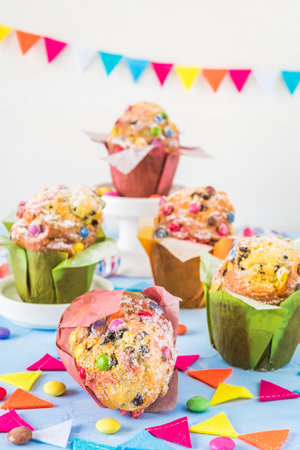 Colorful muffins on blue, decorated with a party garland and chocolate beans for a party, birthday, carnival, new year. Vertical.の写真素材