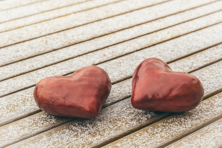 Two red hearts on a wooden table that is lightly covered with snowの写真素材