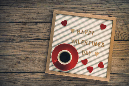 White board with gold lettering for valentines day, red hearts and a red cup of espresso coffee on rustic wooden background, top viewの写真素材