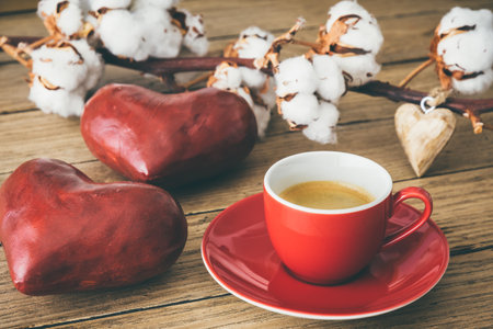 Red cup with espresso coffee on wood, decorated with red big hearts and a cotton branchの写真素材