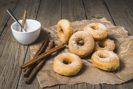 Mini donuts with sugar and cinnamon on a paper on a wooden tableの写真素材