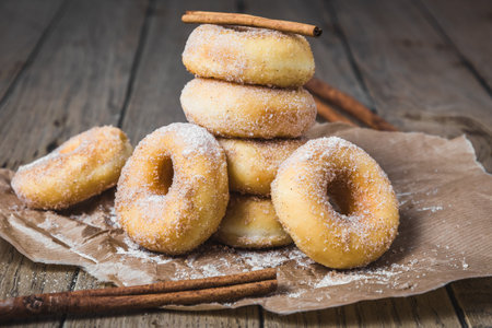 Sugared stacked mini donuts with cinnamon on brown paper on a wooden tableの写真素材