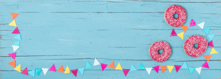 Three pink donuts and a party garland on a turquoise wooden background as bannerの写真素材