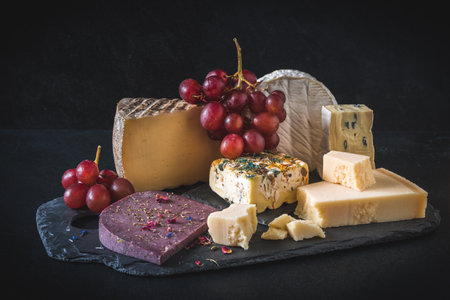 Variety of exclusive and colorful cheese, decorated with red grapes, on black backgroundの写真素材