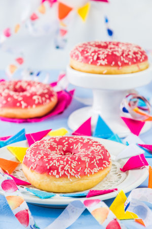 Pink glazed donuts on a light blue background, decorated with streamers and a party garland, verticalの写真素材