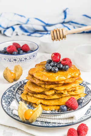 Pile of vegan pancakes with berries and syrup on a blue-white patterned plate on white background, verticalの写真素材