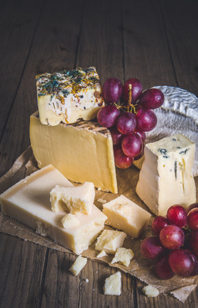 Variety of exclusive cheese, decorated with red grapes, on a rustic wooden table, verticalの写真素材