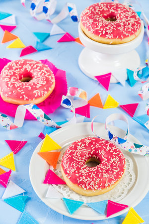 Pink glazed donuts on a light blue background, decorated with streamers and a party garland, verticalの写真素材