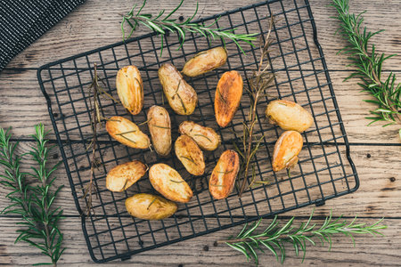 Baked unpeeled halfed potatoes with salt and rosemary on a black cooling rack on a rustic wooden table, top viewの写真素材