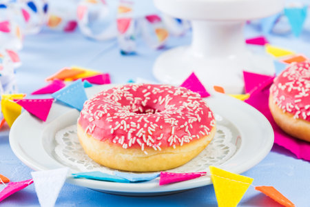 Pink glazed donut on a white plate on a light blue background, decorated with a streamer and party garlandの写真素材