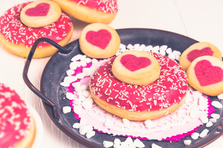 Pink glazed donut and cookies with hearts on a metal tray on a white tableの写真素材