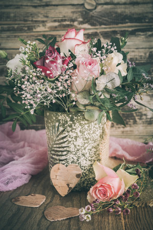 Vase with flower bouquet with pink and white roses on wooden background, vintage style, verticalの写真素材