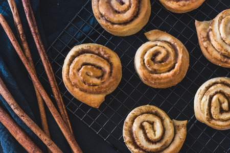 Homemade cinnamon rolls on a cooling rack with cinnamon sticks on dark blue background, top viewの写真素材