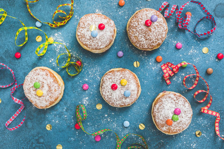 Krapfen, Berliner or donuts with streamers, confetti and chocolate beans on blue background. Colorful carnival or birthday image, top view.の写真素材